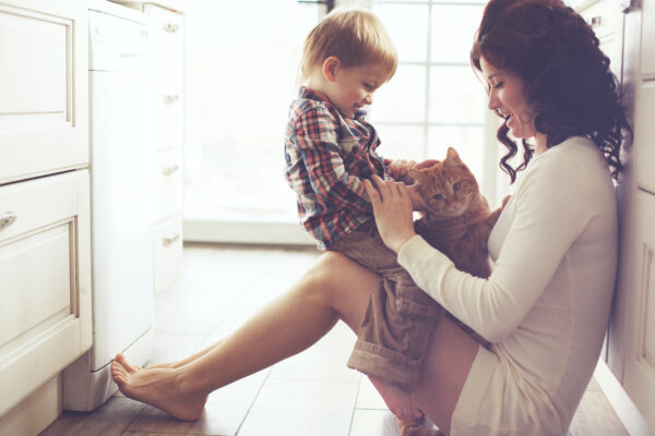 Mother with her toddler boy of potty-training age playing with pet on the floor at the kitchen at home