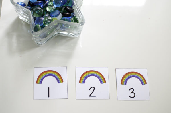 rainbow counting cards with numbers printed on them next to a container of glass gems