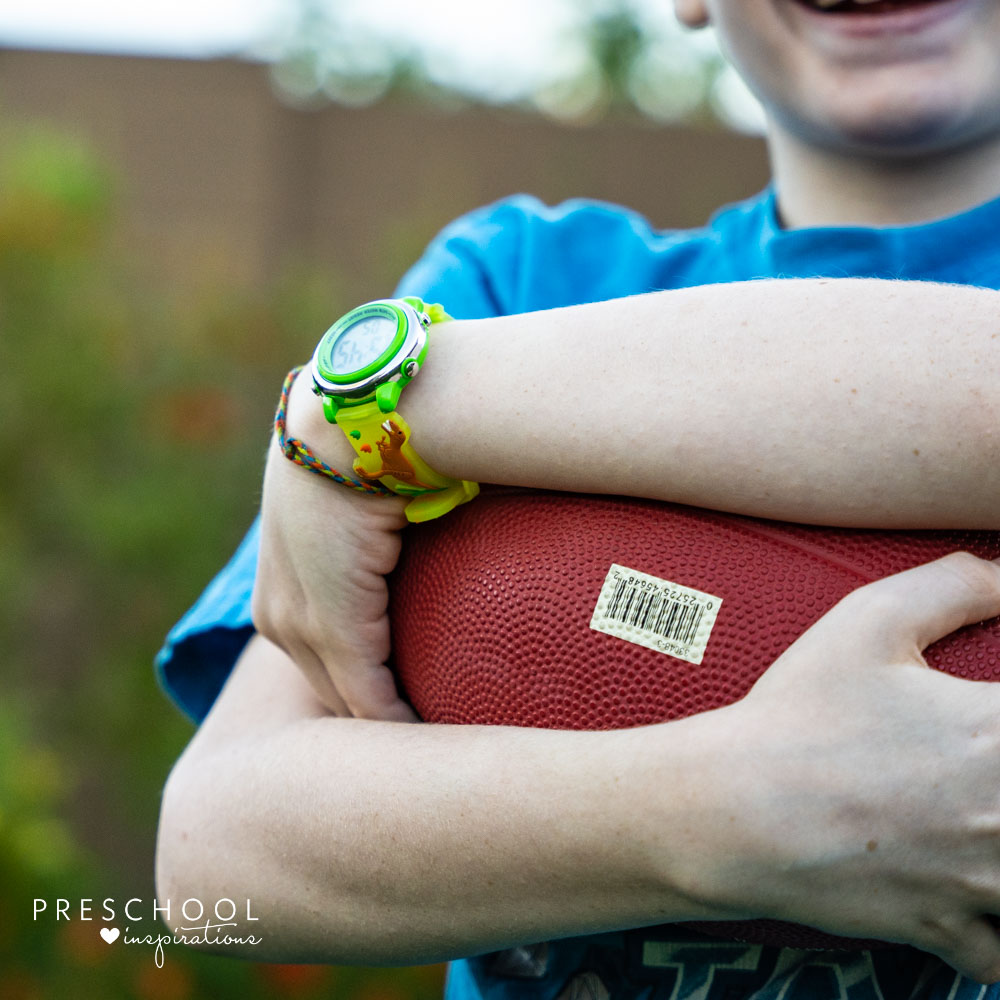 Boy holding a football while wearing a digital watch.