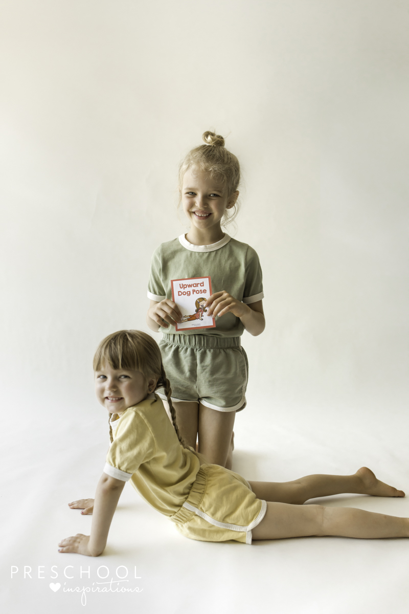 One girl doing upward dog pose and a girl holding the card behind her